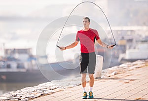 Young man wearing sportswear skipping rope at quay during autumn