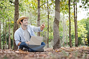 A young man wearing a straw hat happily uses a notebook while working in the forest garden.