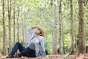 A young man wearing a straw hat relaxes in a garden filled with trees.