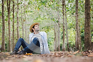A young man wearing a straw hat relaxes in a garden filled with trees.