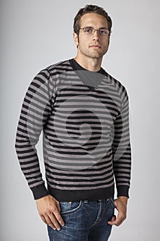 Young man wearing striped sweater, denim jeans and eyeglasses. Men`s casual fall clothing apparel fashions styles.