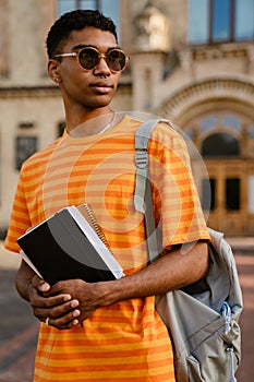 Young man wearing sunglasses holding notepad while walking outdoors