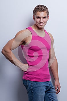 young man wearing undershirt and jeans, posing at white wal