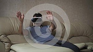 Young man wearing virtual reality glasses and sitting on sofa at home.