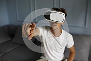 Young man wearing virtual reality goggles in modern coworking interior sitting on sofa. Smartphone using with VR headset. 3D
