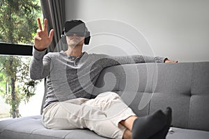 Man wearing virtual reality headset playing video game or watching movie on sofa at home.