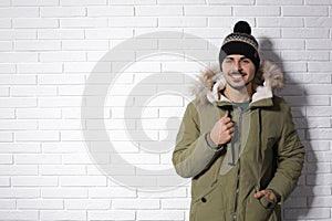 Young man wearing warm clothes against brick wall, space for text. Ready for winter