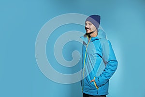Young man wearing warm clothes on color background, space for text. Ready for winter
