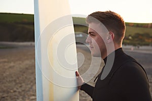 Young Man Wearing Wetsuit Enjoying Surfing Staycation On Beach As Sun Sets