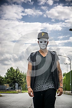 Young man wearing white creepy mask outdoor in city street