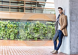 Young man wearing winter clothes in the street. Young guy with modern hairstyle with coat, blue jeans and white sweeter