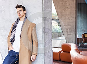 Young man wearing winter clothes in the street. Young guy with modern hairstyle with coat, blue jeans and white sweeter