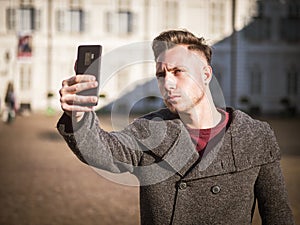 Young man wearing winter coat taking selfie photo with his smartphone