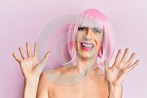 Young man wearing woman make up wearing pink wig afraid and terrified with fear expression stop gesture with hands, shouting in