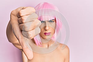 Young man wearing woman make up wearing pink wig looking unhappy and angry showing rejection and negative with thumbs down gesture