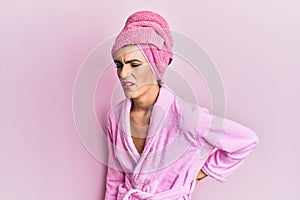 Young man wearing woman make up wearing shower towel on head and bathrobe suffering of backache, touching back with hand, muscular
