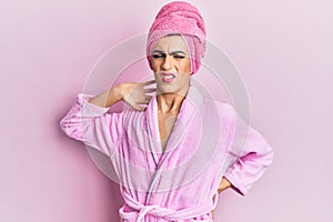 Young man wearing woman make up wearing shower towel on head and bathrobe suffering of neck ache injury, touching neck with hand,
