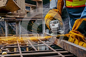 Young man welder in a working blue overall and working gloves grinds a metal object with a angle grinder in the garage,