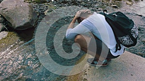 Young man wets his head in a clean, cool mountain stream.