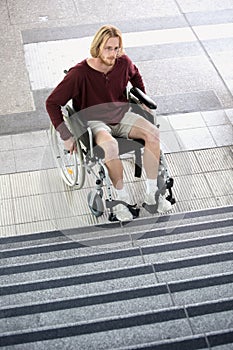 Young man in wheel chair in front of stairs looking sad