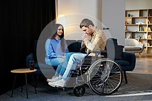 Young man in a wheelchair. Girlfriend comforting her sad boyfriend