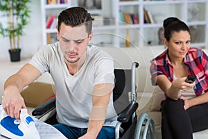 Young man on wheelchair ironing at home