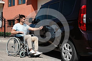 Young man in wheelchair opening  of his van outdoors