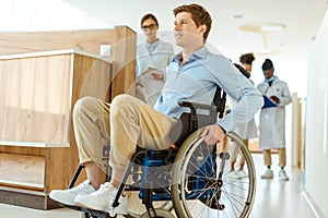Young man in wheelchair rolling down a hospital corridor with doctors