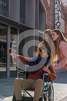 Young man in a wheelchair taking a selfie with a mobile together with two young girls