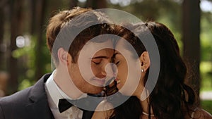Young man whispering on ear outdoors. Sweet bride and groom hugging in park
