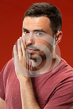 The young man whispering a secret behind her hand over red background