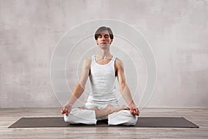 Young man in white clothes doing yoga in living room