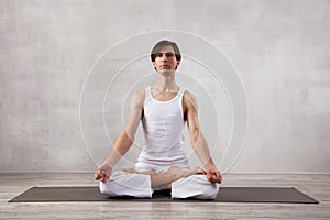 Young man in white clothes doing yoga in living room