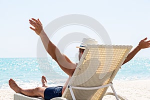 Young man in white hat relaxing in deck chair on beautiful sandy beach