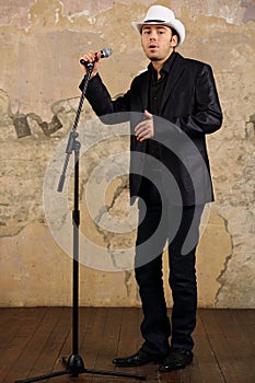 Young man in white hat and suit sings into photo