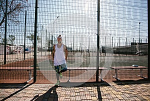 Young man with white headband on his head and tattoos on his arms dressed in the white t-shirt, black leggings and blue