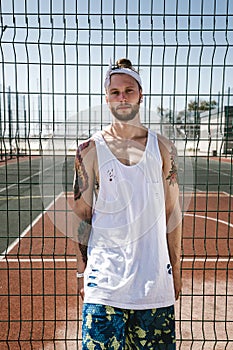 Young man with white headband on his head and tattoos on his arms dressed in the white t-shirt, black leggings and blue