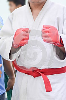 Young man in white kimono for sambo, judo, jujitsu posing on white background, looking straight, position of fighting post, hands
