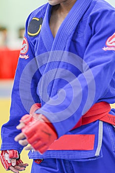 Young man in white kimono for sambo, judo, jujitsu posing on white background, looking straight, position of fighting post, hands