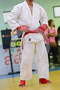 Young man in white kimono for sambo, judo, jujitsu posing on white background, looking straight, position of fighting post, hands