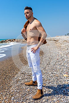 Young man in white pants and modern styling posing on the beach of the Mediterranean Sea in Burriana