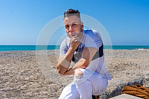 Young man in white pants and modern styling posing on the beach of the Mediterranean Sea in Burriana