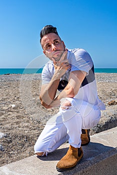 Young man in white pants and modern styling posing on the beach of the Mediterranean Sea in Burriana