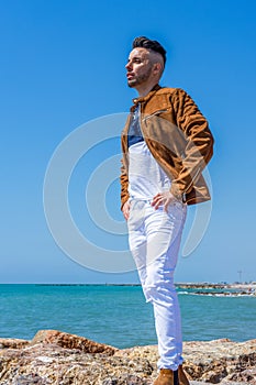 Young man in white pants and modern styling posing on the beach of the Mediterranean Sea in Burriana