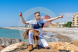 Young man in white pants and modern styling posing on the beach of the Mediterranean Sea in Burriana