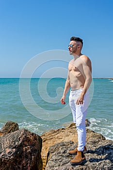 Young man in white pants and modern styling posing on the beach of the Mediterranean Sea in Burriana