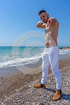 Young man in white pants and modern styling posing on the beach of the Mediterranean Sea in Burriana