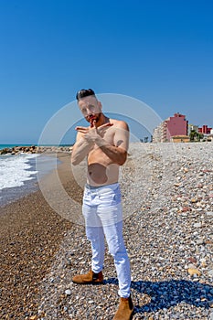 Young man in white pants and modern styling posing on the beach of the Mediterranean Sea in Burriana