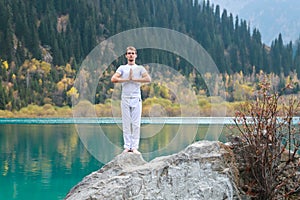 A young man in white practices yoga in the mountains lake. Pose Samasthiti namaskar