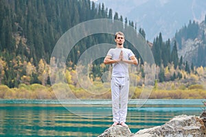A young man in white practices yoga in the mountains. Pose Samasthiti namaskar